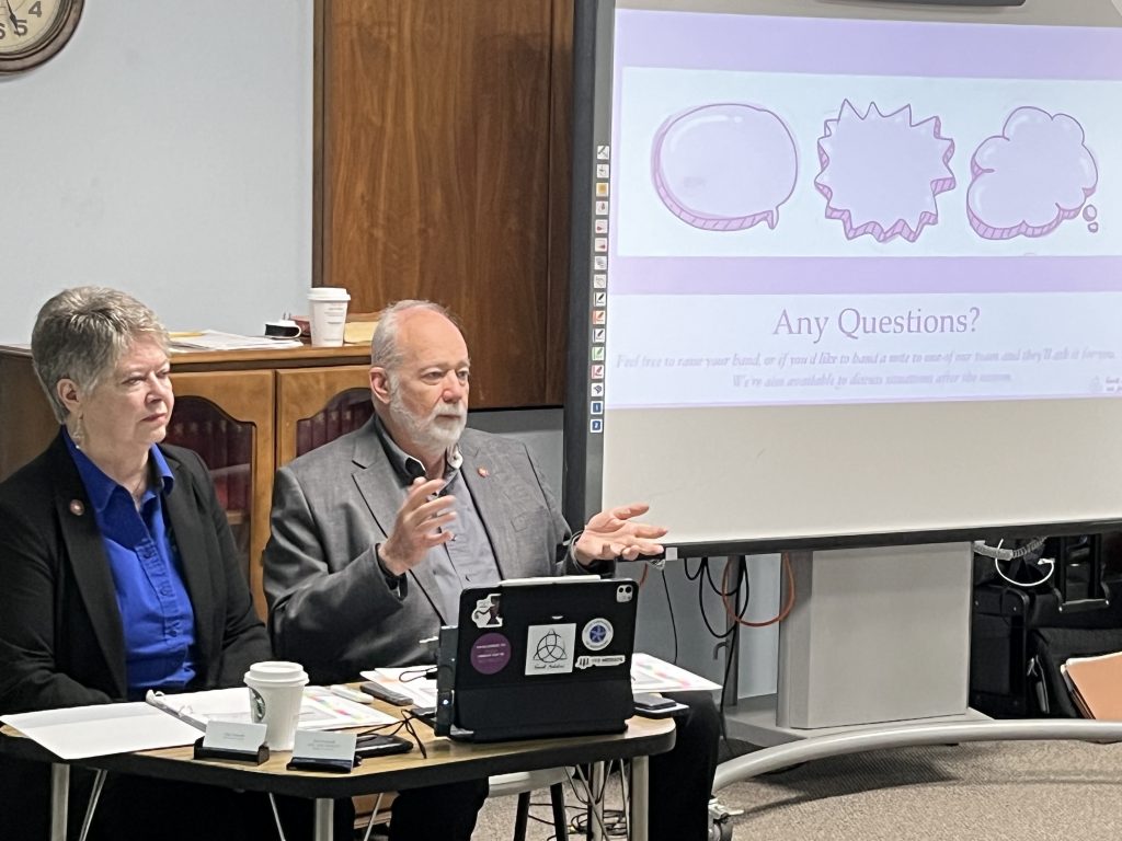Terri Francell and Clay Francell speaking at the free information session with a slide on the screen asking "Any Questions?"